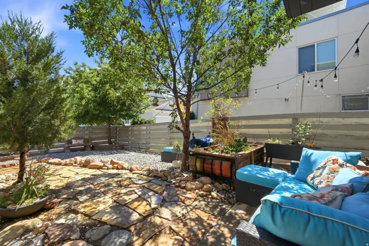 Outdoor patio featuring flagstone paving, integrated gravel landscaping, mature trees, a wooden privacy fence, and string lighting