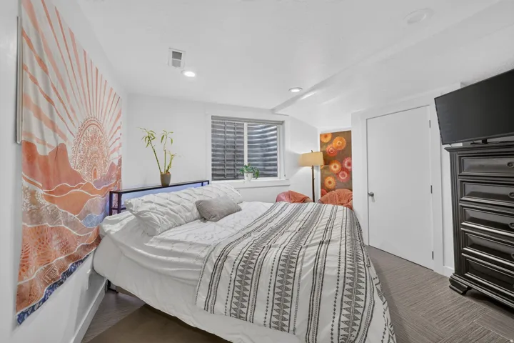 Recessed lighting illuminates this room, featuring wood-finish flooring and a window with horizontal blinds
