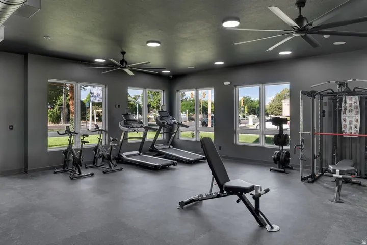 Fitness center featuring extensive cardio equipment, strength training apparatus, a durable rubber floor, multiple ceiling fans, and abundant natural light from large windows