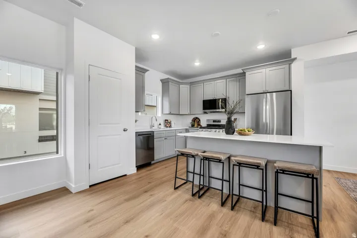 Modern kitchen featuring gray cabinetry, stainless steel appliances, white countertops, and wood-finish flooring