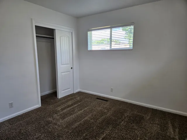 Interior room featuring a sliding closet door with a textured panel, white trim, and a window with blinds