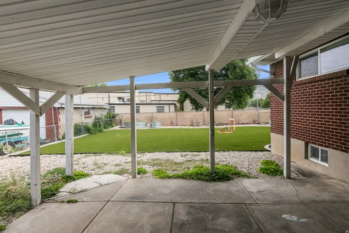 Covered concrete patio overlooking a backyard with artificial turf and a gravel border