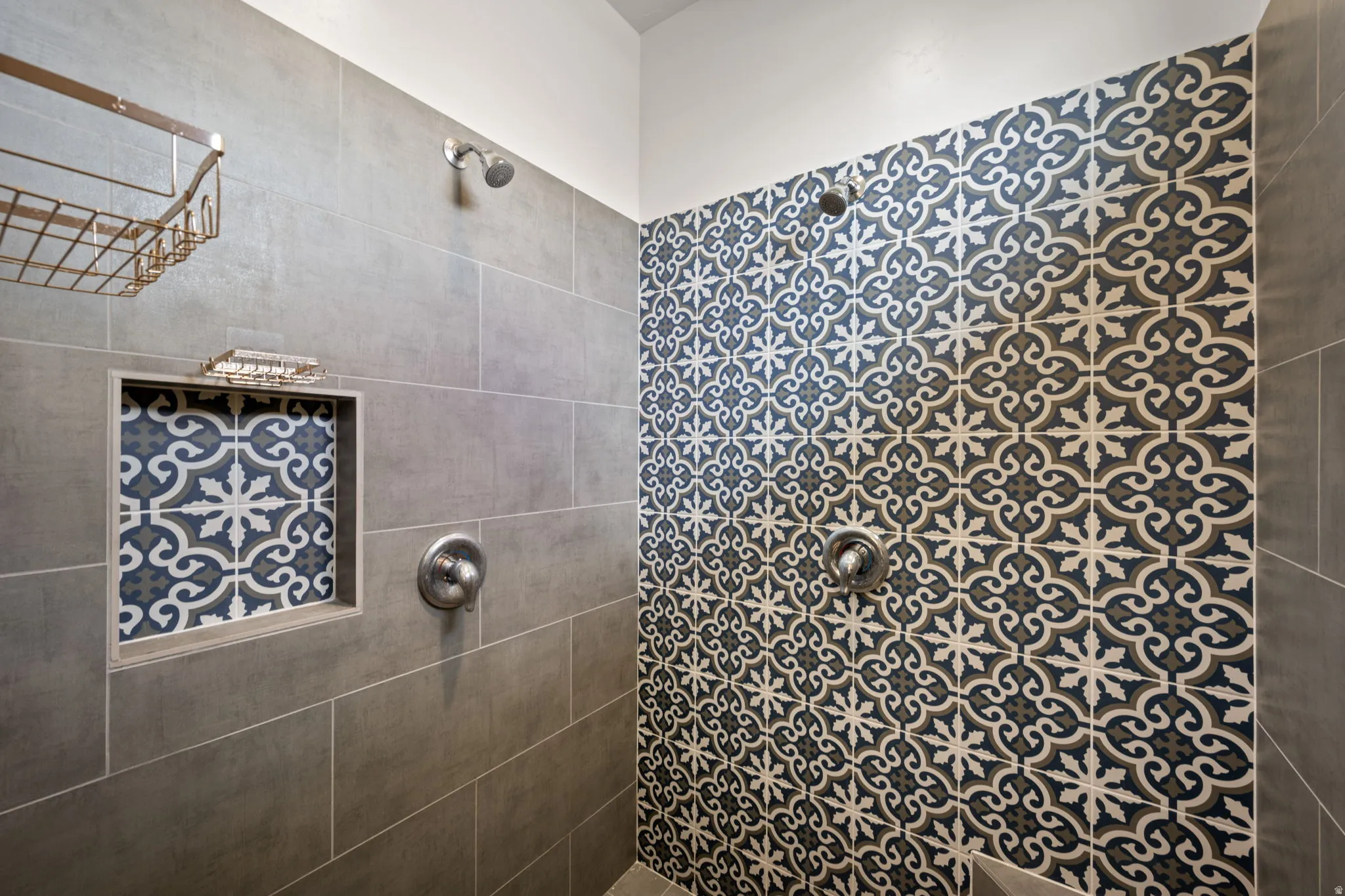 Shower stall featuring patterned wall tile, contrasting gray wall tile, a built-in shower niche with patterned tile backing, a fixed showerhead, and a shower control