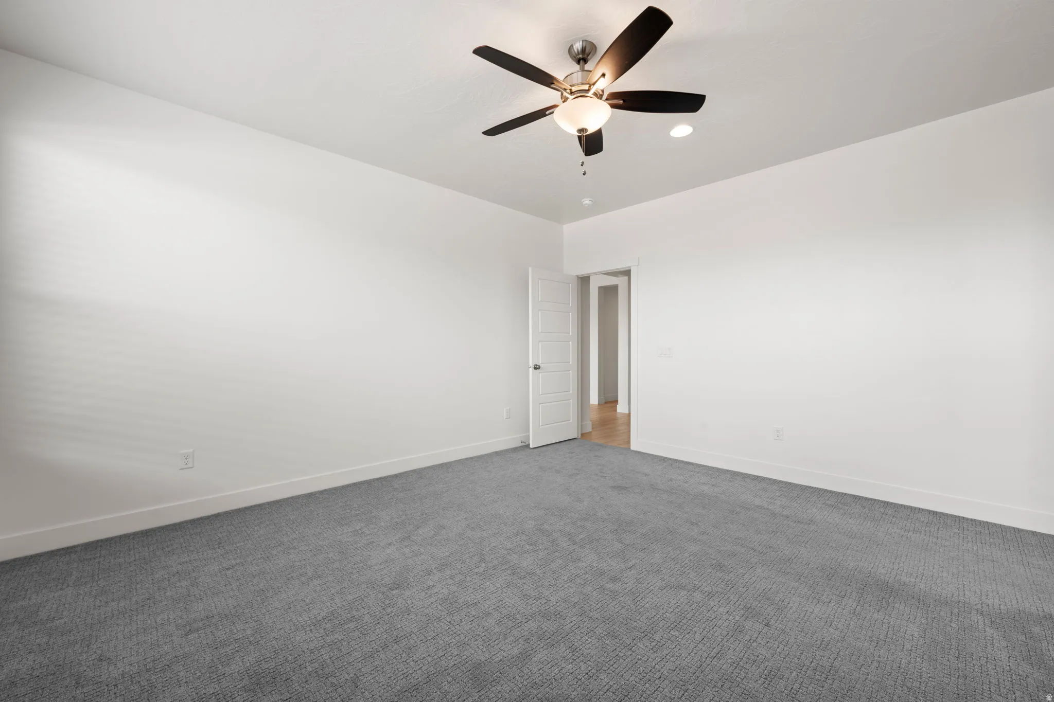 Spacious room featuring neutral white walls, plush gray carpeting, and a modern ceiling fan with integrated lighting