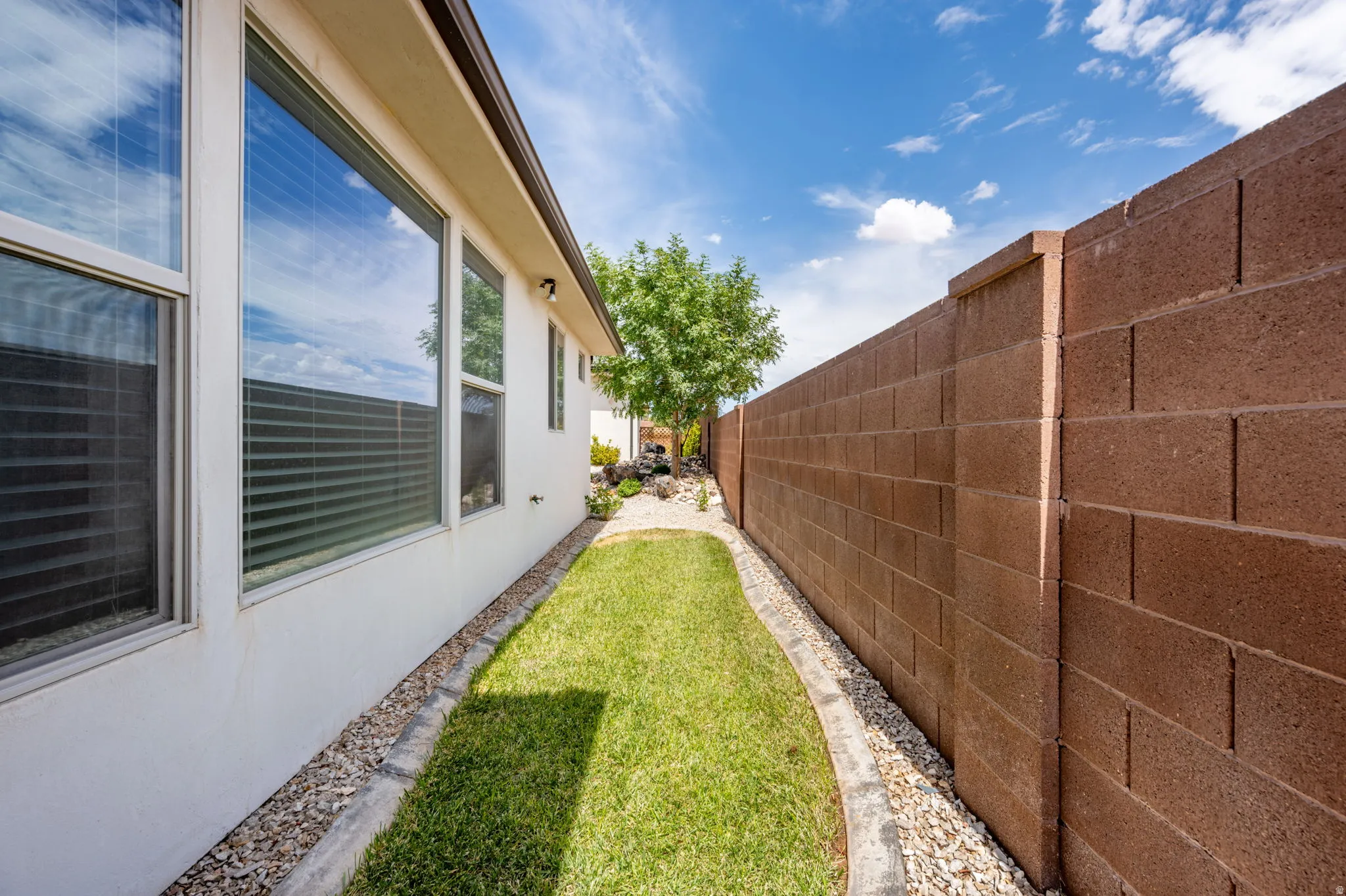 Exterior stucco wall with multiple windows, a block wall boundary, and a landscaped strip featuring grass and gravel