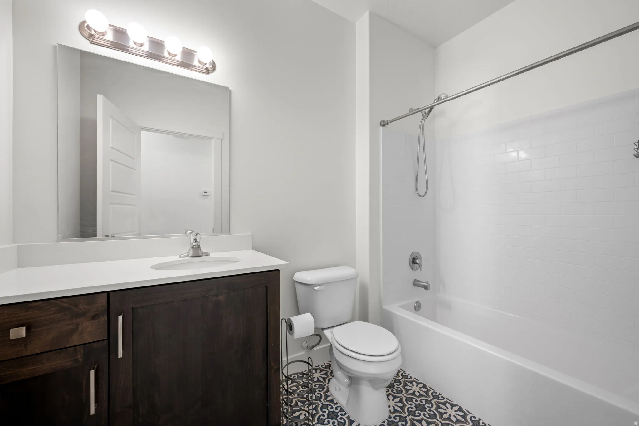 Bathroom featuring a dark wood-finish vanity with a light countertop, a subway-tiled tub/shower combination, and patterned floor tiling