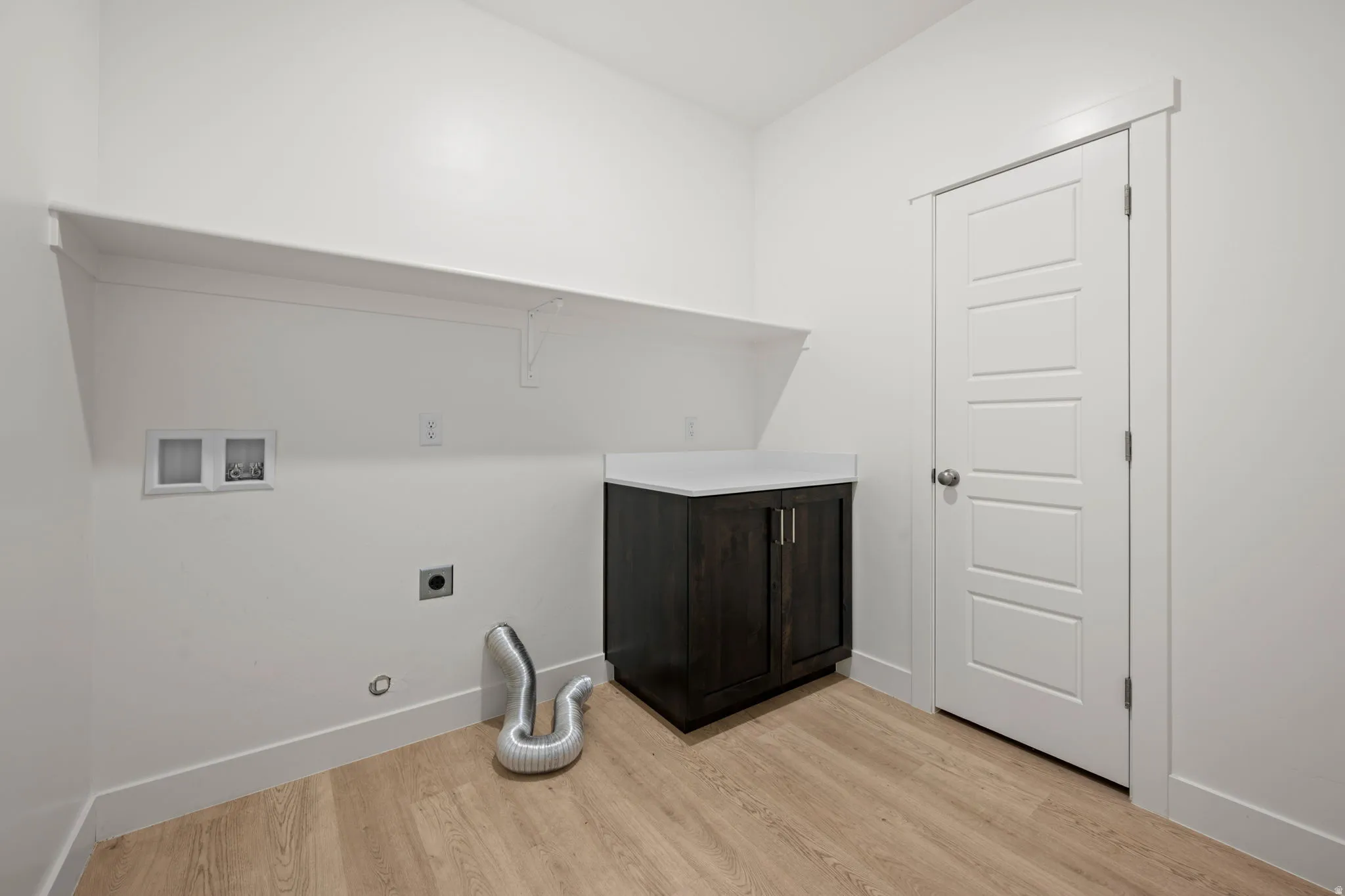 Laundry room featuring wood-finish flooring, a dark wood-finish vanity with a white countertop, and a white paneled door