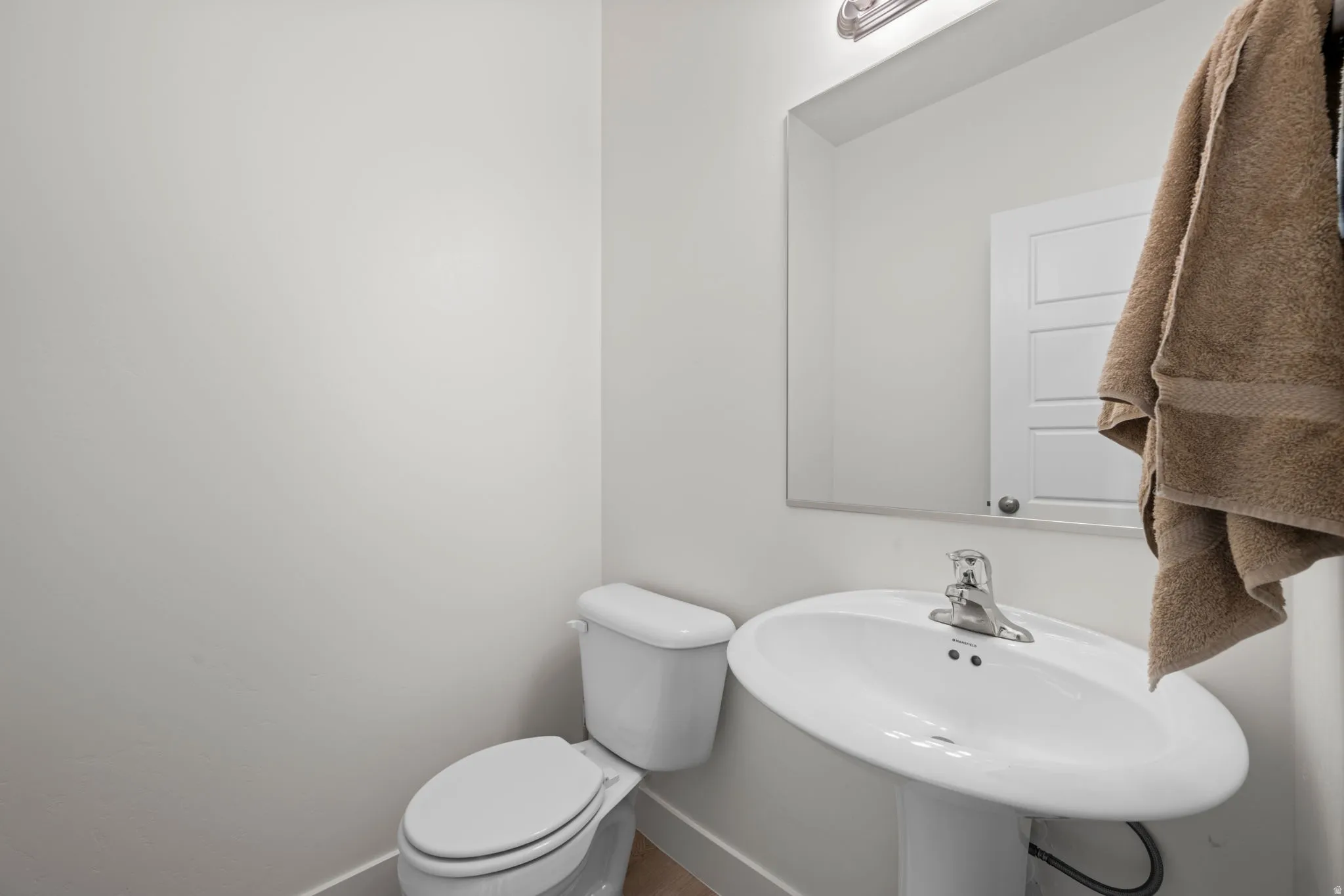 Pedestal sink with chrome faucet, mirror with overhead vanity lighting, and white toilet