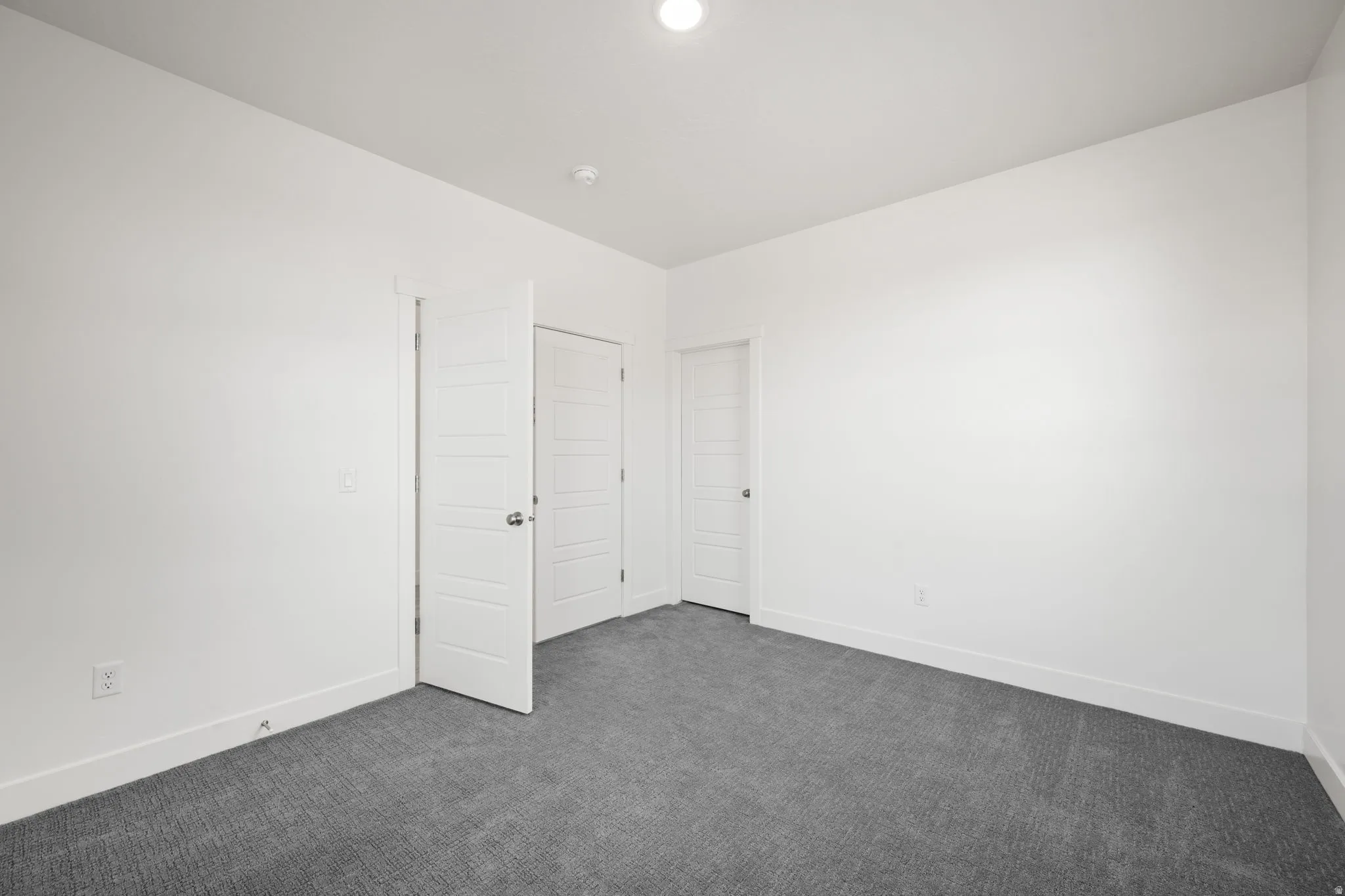 Spacious room featuring neutral white walls and dark gray patterned carpeting