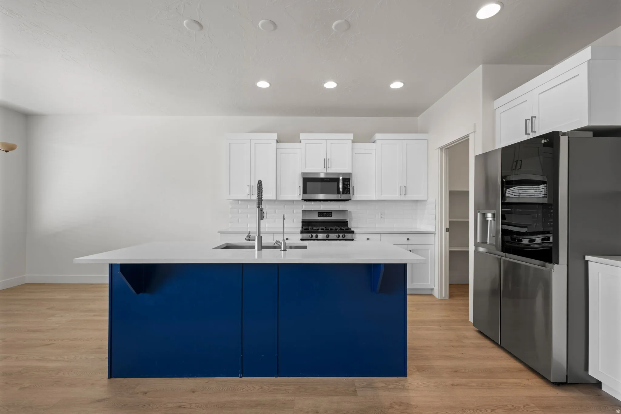 Kitchen featuring a distinctive blue island with a large sink, white shaker cabinetry, stainless steel appliances, and wood-finish flooring