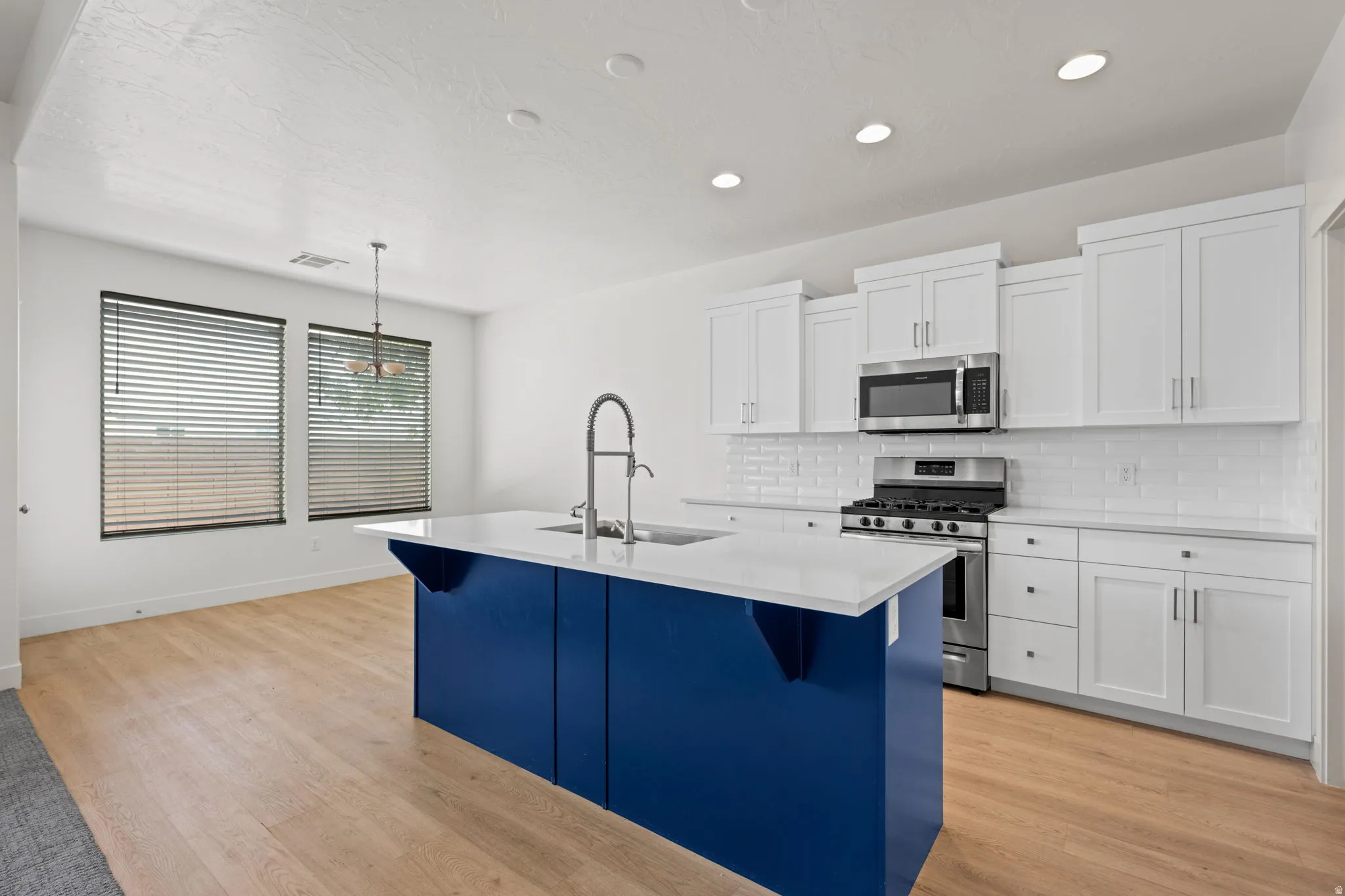 Kitchen featuring a blue island with a white countertop, stainless steel appliances, white subway tile backsplash, white cabinetry, and wood-finish flooring