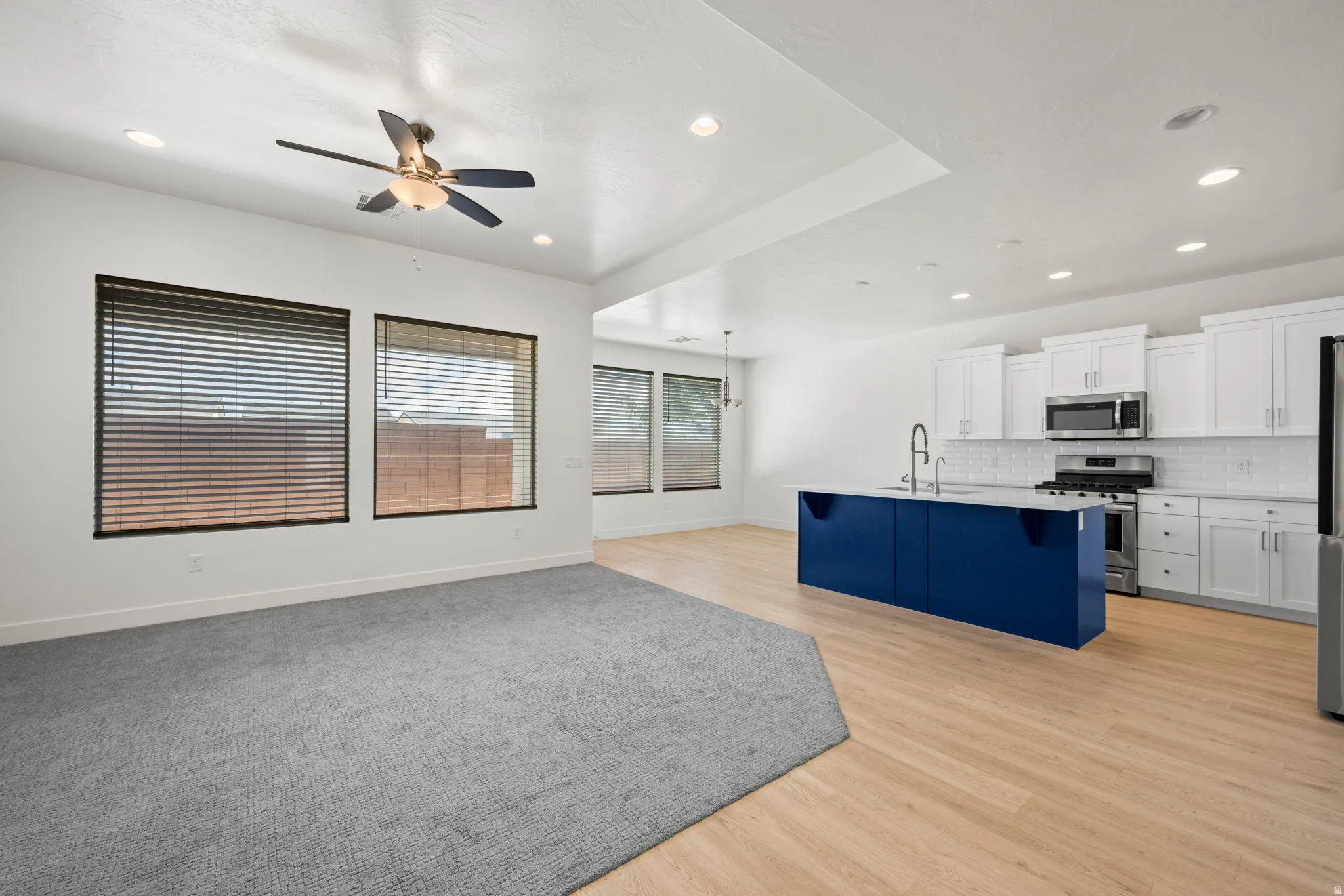 Open-concept living space featuring a contemporary kitchen with white shaker cabinetry, stainless steel appliances, and a bold blue island with a contrasting countertop