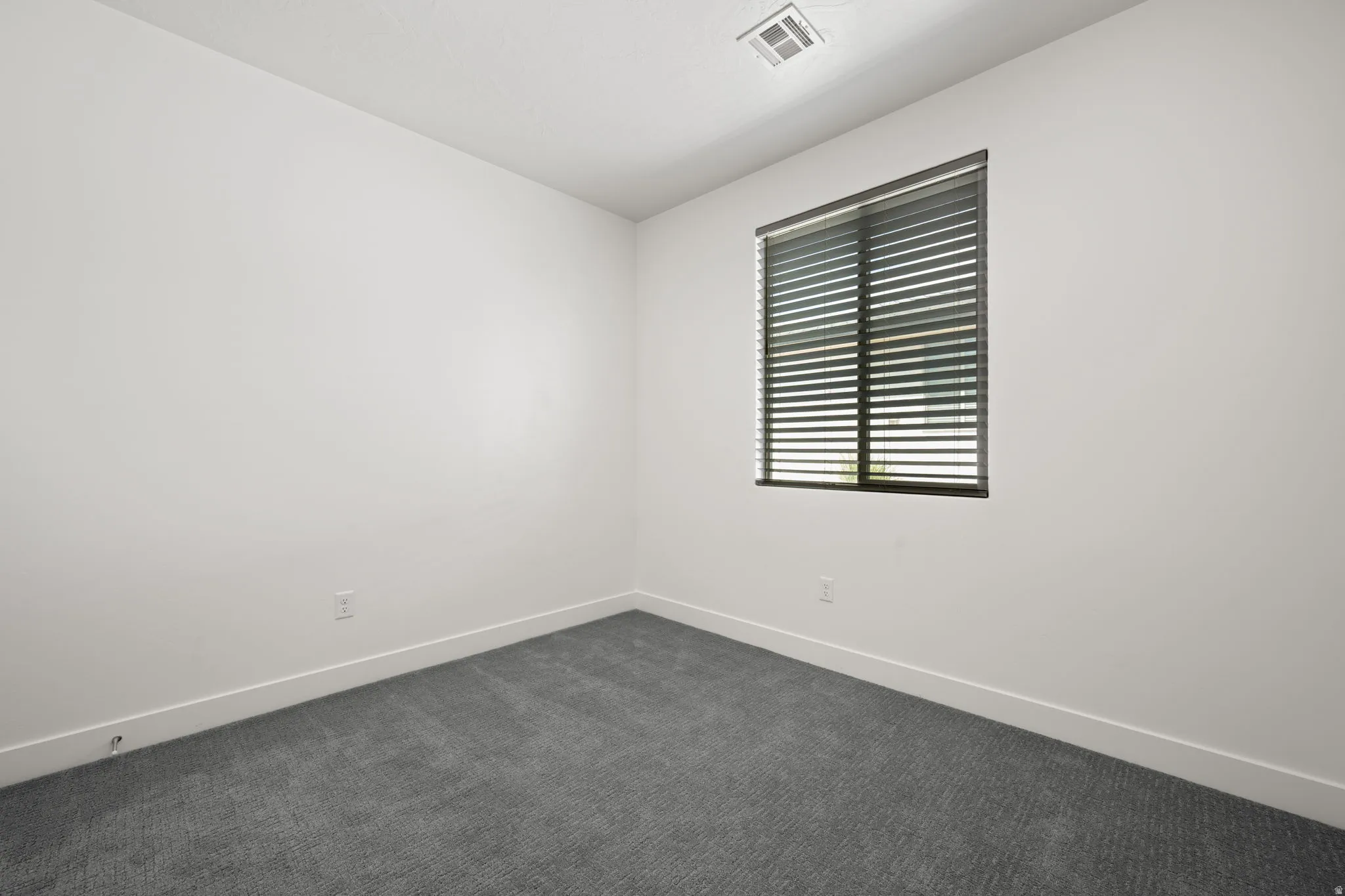 Bedroom featuring neutral-toned walls, grey carpet, a single window with horizontal blinds, and clean white baseboards