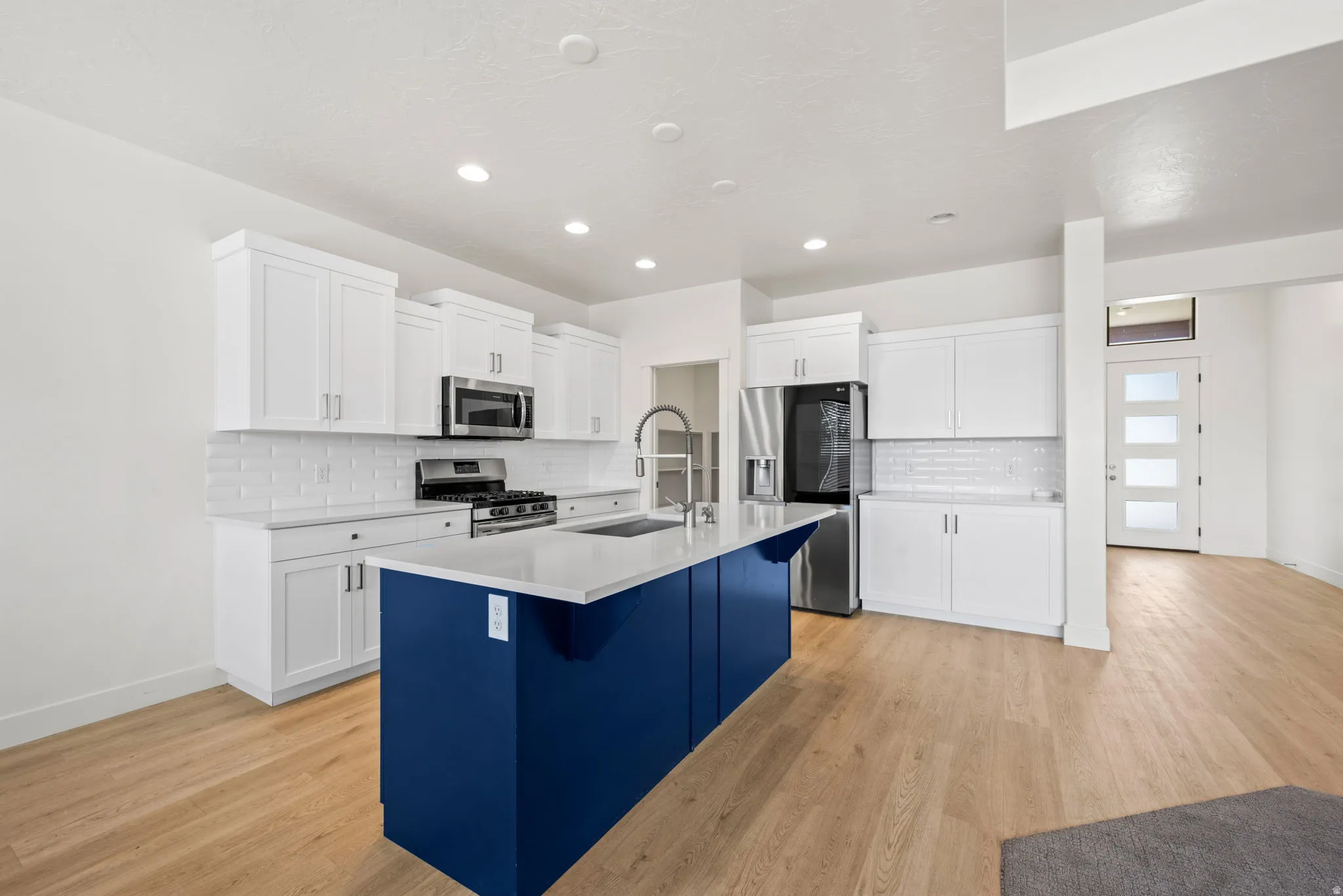 Kitchen featuring a blue island with a light-toned countertop, white shaker-style cabinetry, stainless steel appliances, and a white subway tile backsplash