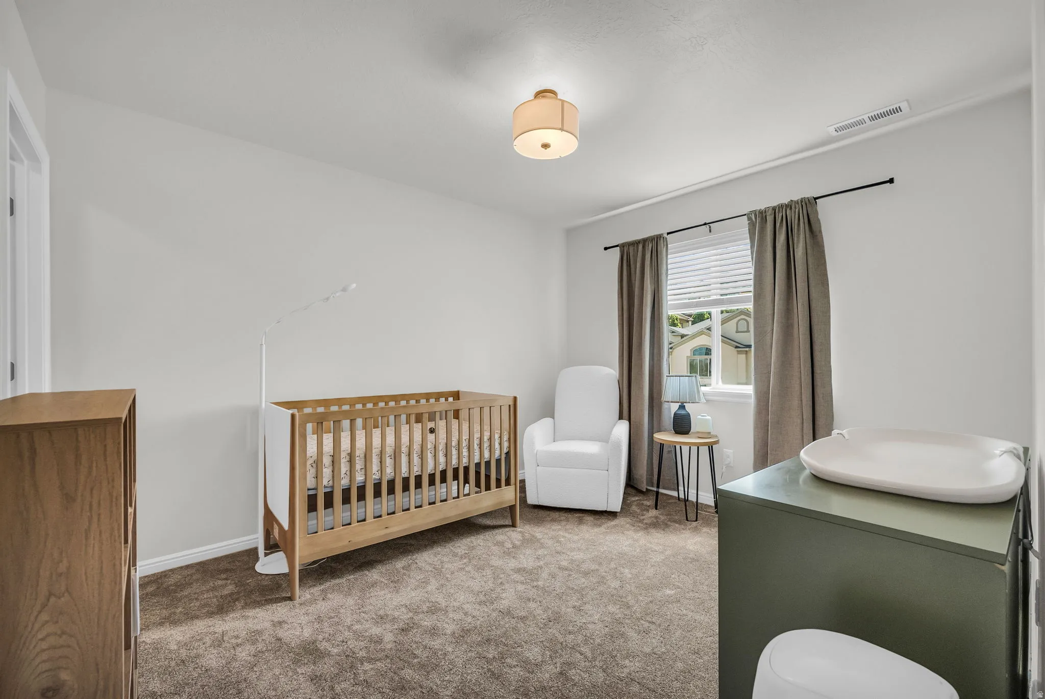 Bright room featuring neutral wall tones, plush carpeting, a single window with blinds and drapes, and a ceiling-mounted light fixture
