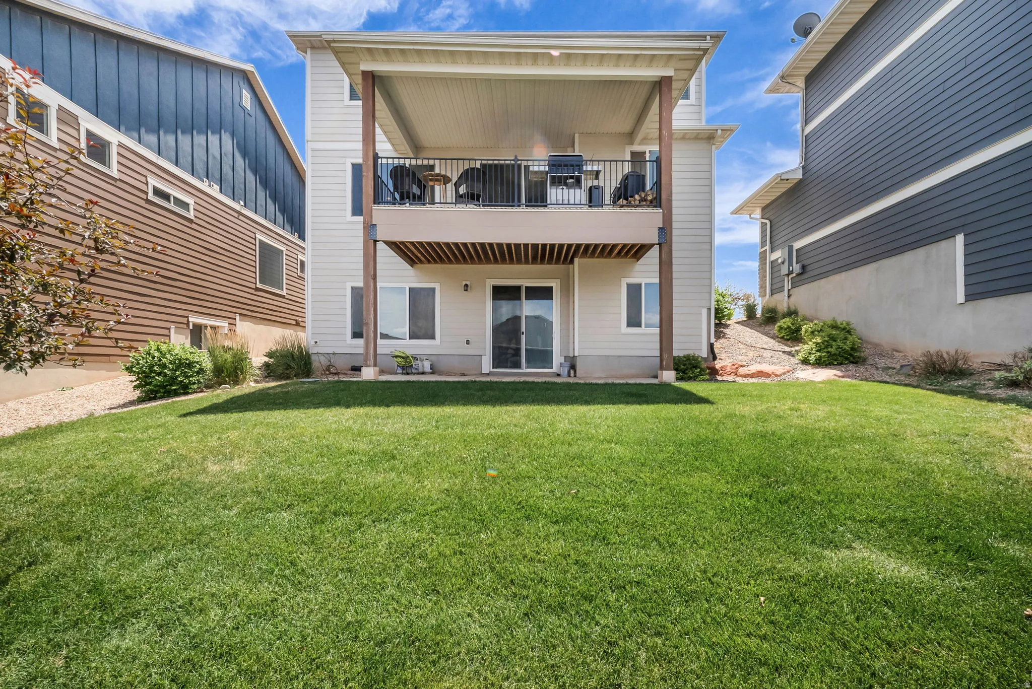 Rear exterior featuring an upper-level covered deck with black railings, a lower-level sliding glass door, and a ground-level patio
