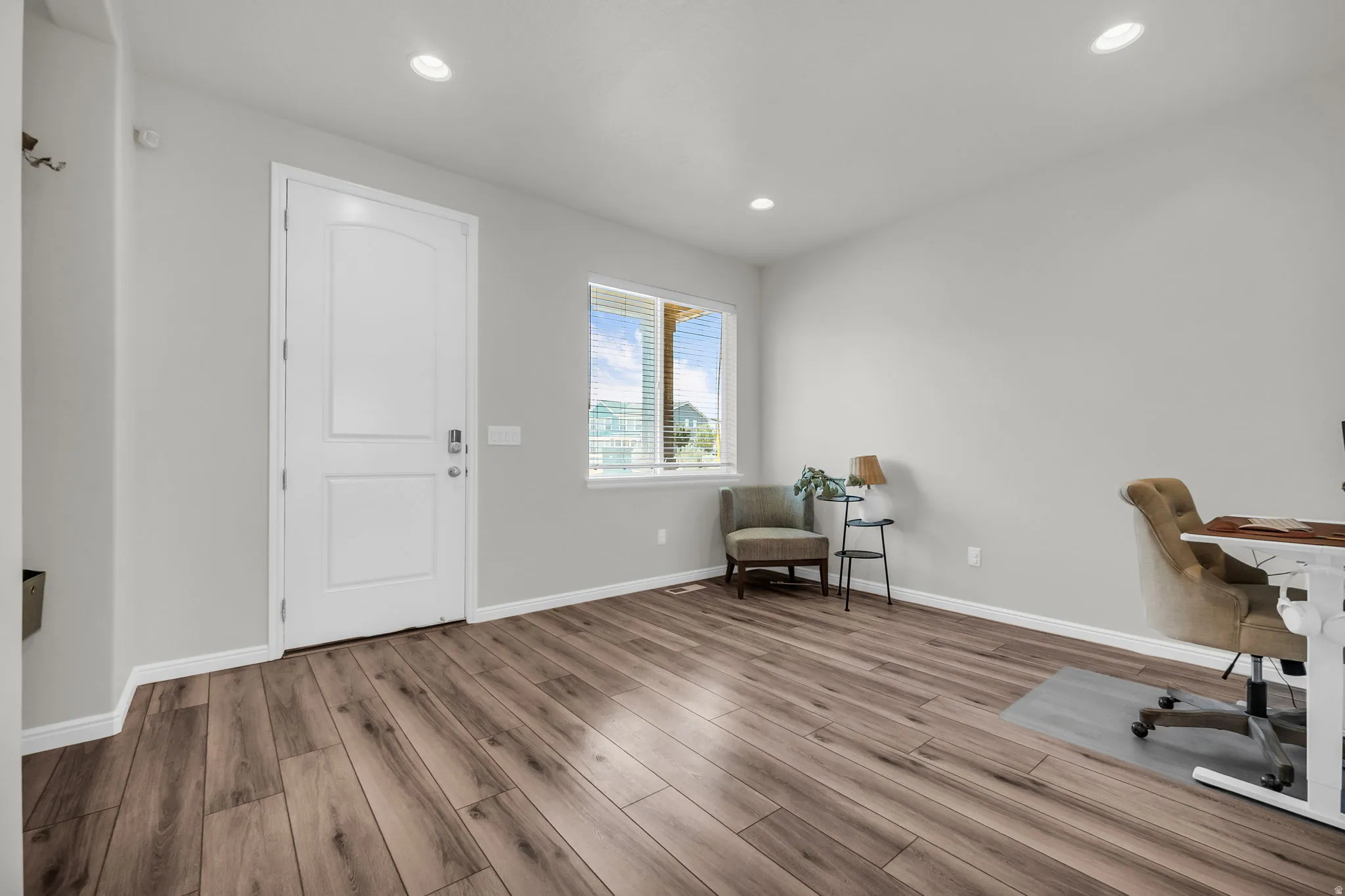 Spacious room featuring wood-finish flooring, recessed lighting, and a white paneled entry door