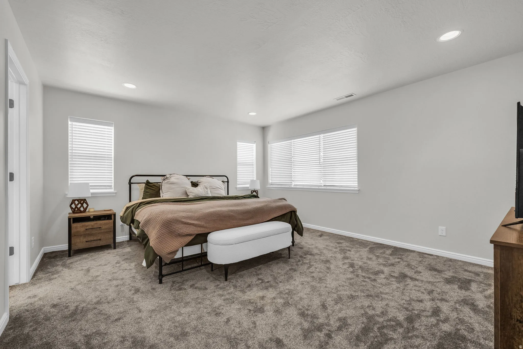 Spacious room featuring neutral-toned walls, recessed lighting, multiple windows with blinds, and plush carpet flooring