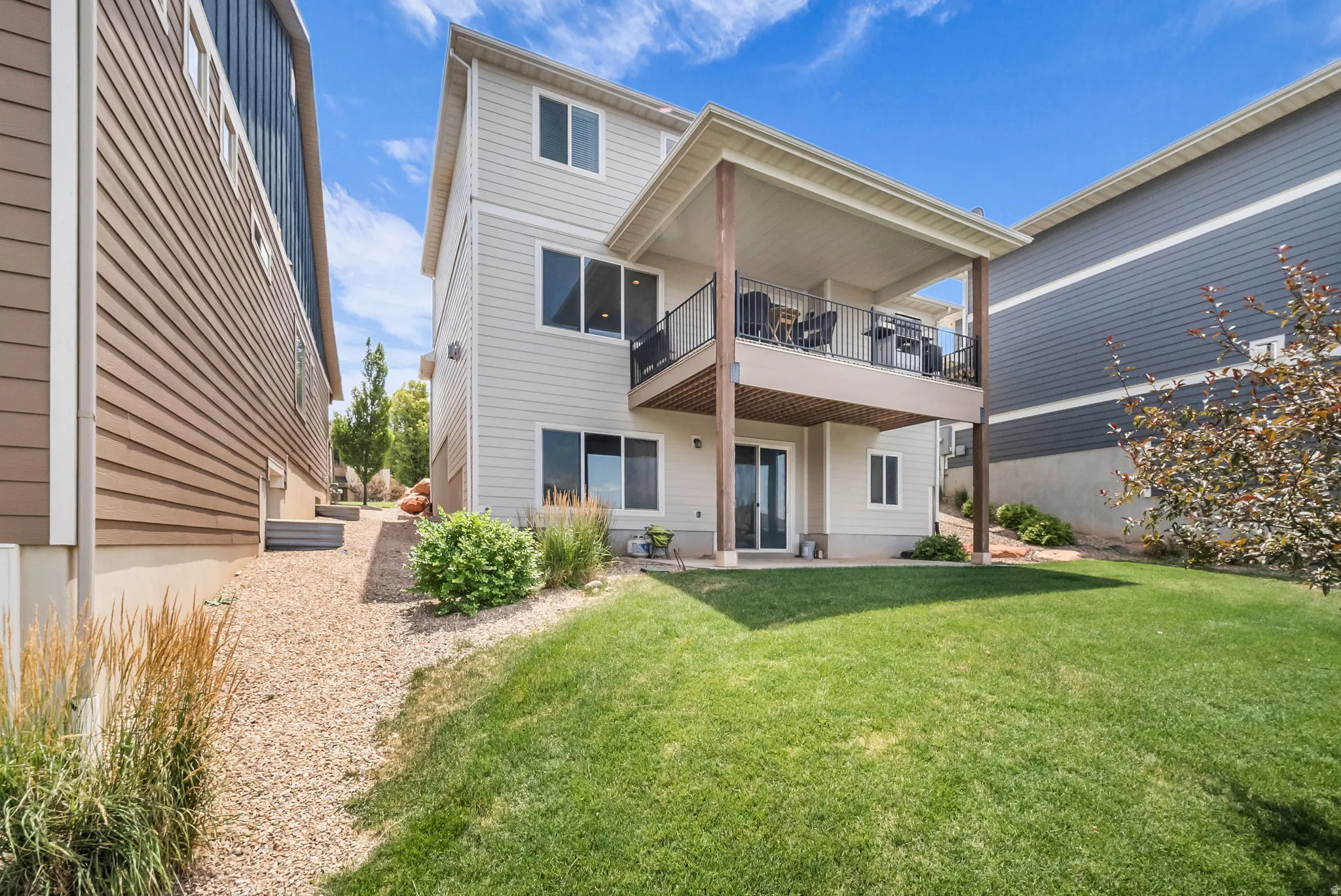 Rear exterior showcasing a covered upper deck with black railings, a lower patio, and a sliding glass door