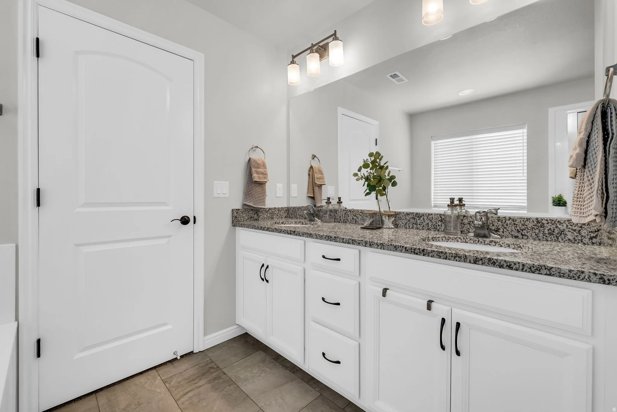 Dual vanity with granite countertops, undermount sinks, and white cabinetry