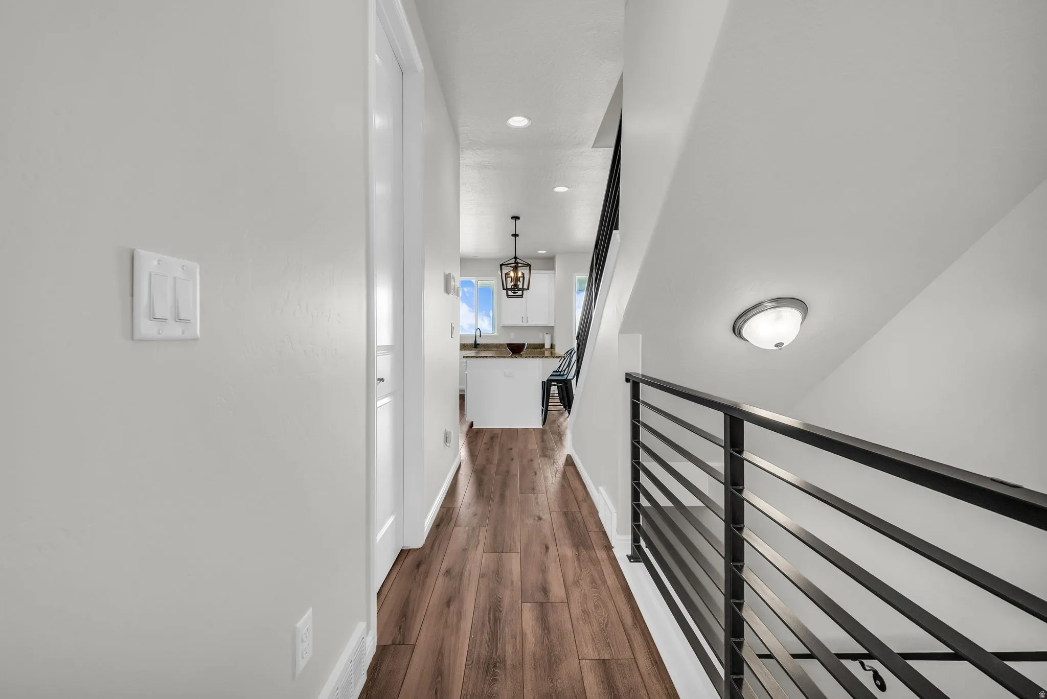 Hardwood-finish flooring extending through the hallway, leading towards a kitchen with white cabinetry and a window