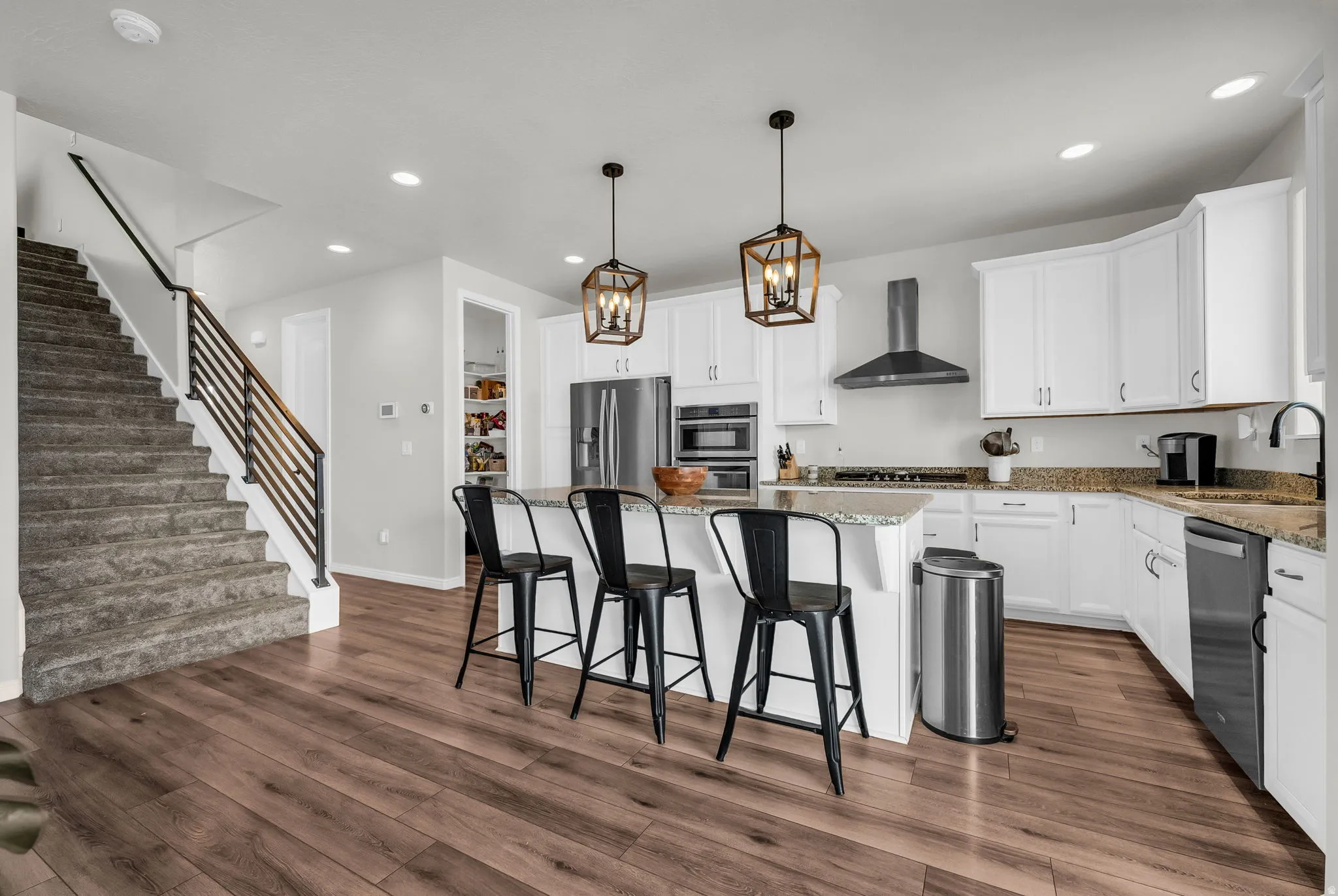 Open-concept kitchen featuring white cabinetry, stainless steel appliances, granite countertops, and a central island with pendant lighting