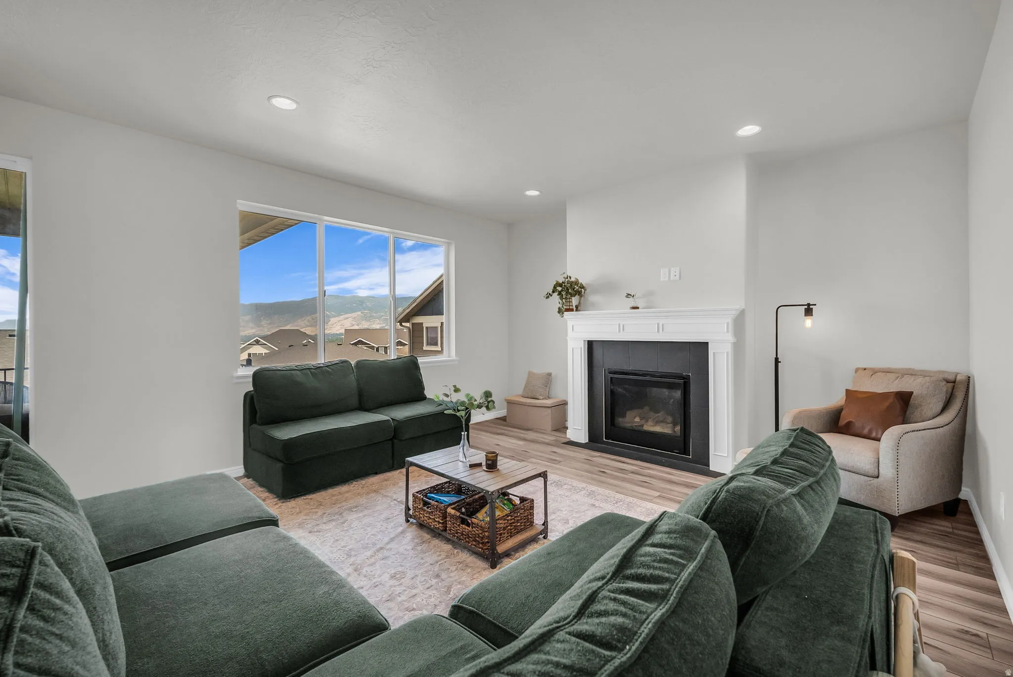 Spacious living area featuring large windows, wood-finish flooring, recessed lighting, and a built-in fireplace with a decorative mantel and dark surround