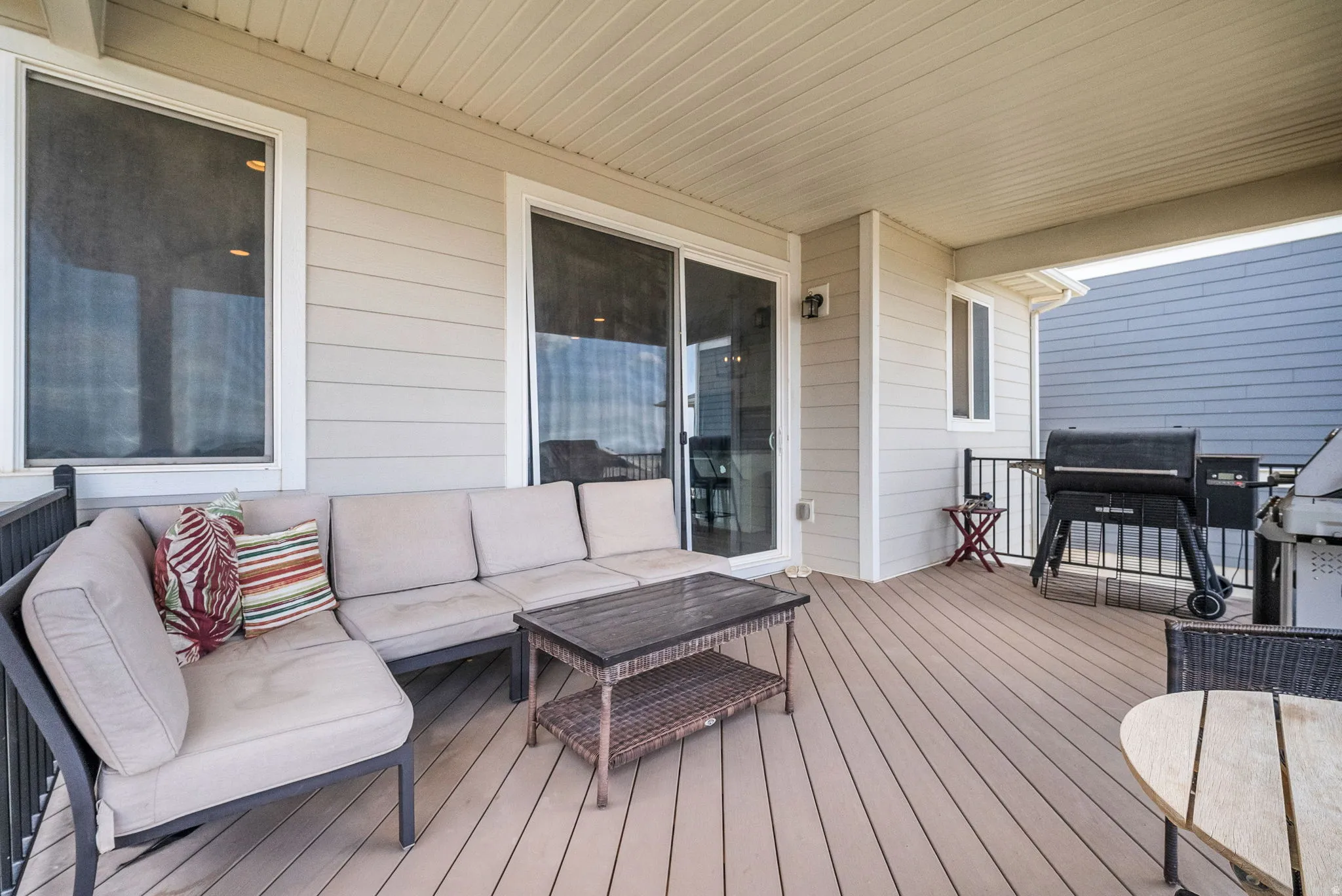 Spacious covered deck featuring composite decking, white vinyl siding, a sliding glass door, and a black metal railing