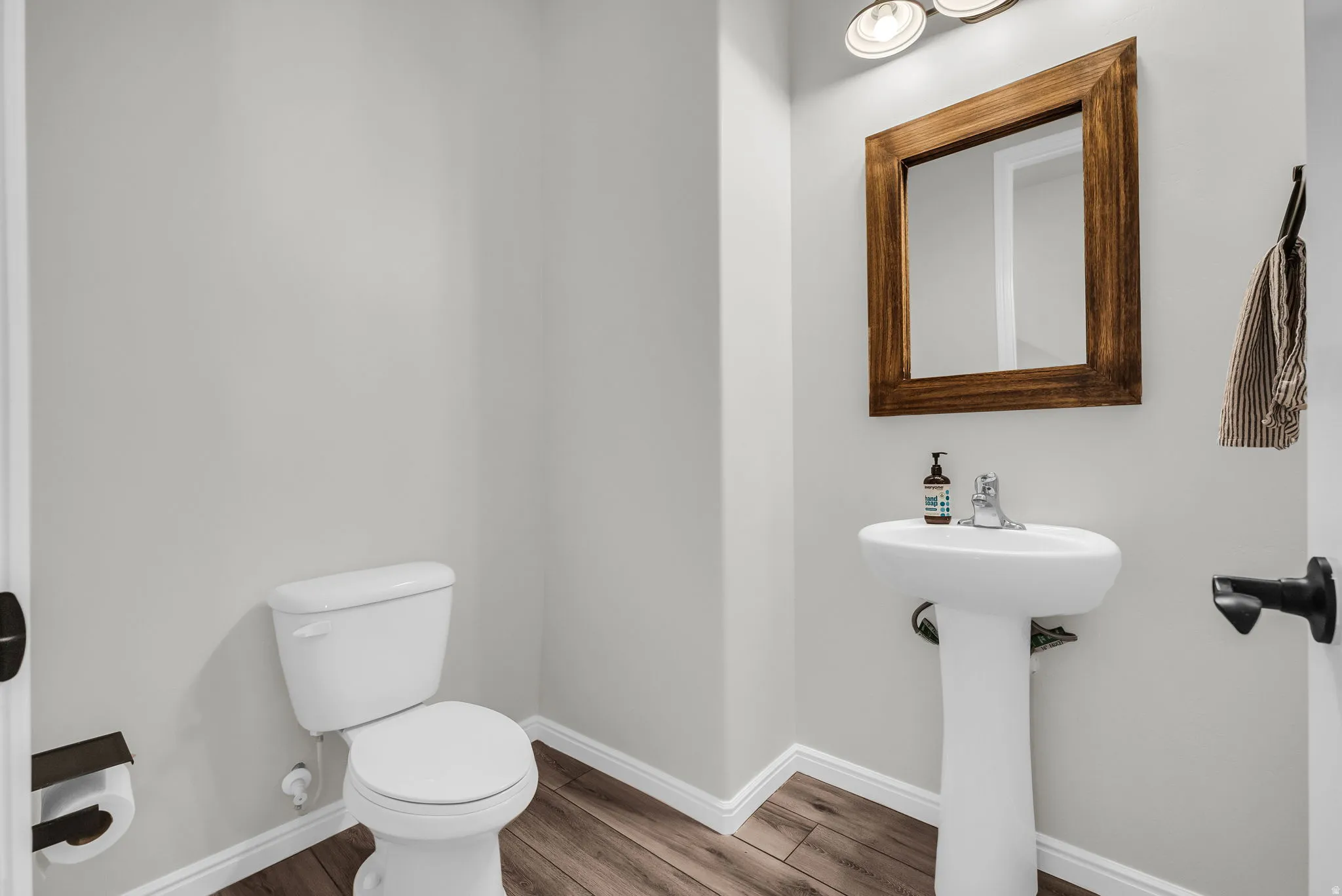 Powder room featuring a pedestal sink, a wood-framed mirror, and a white toilet
