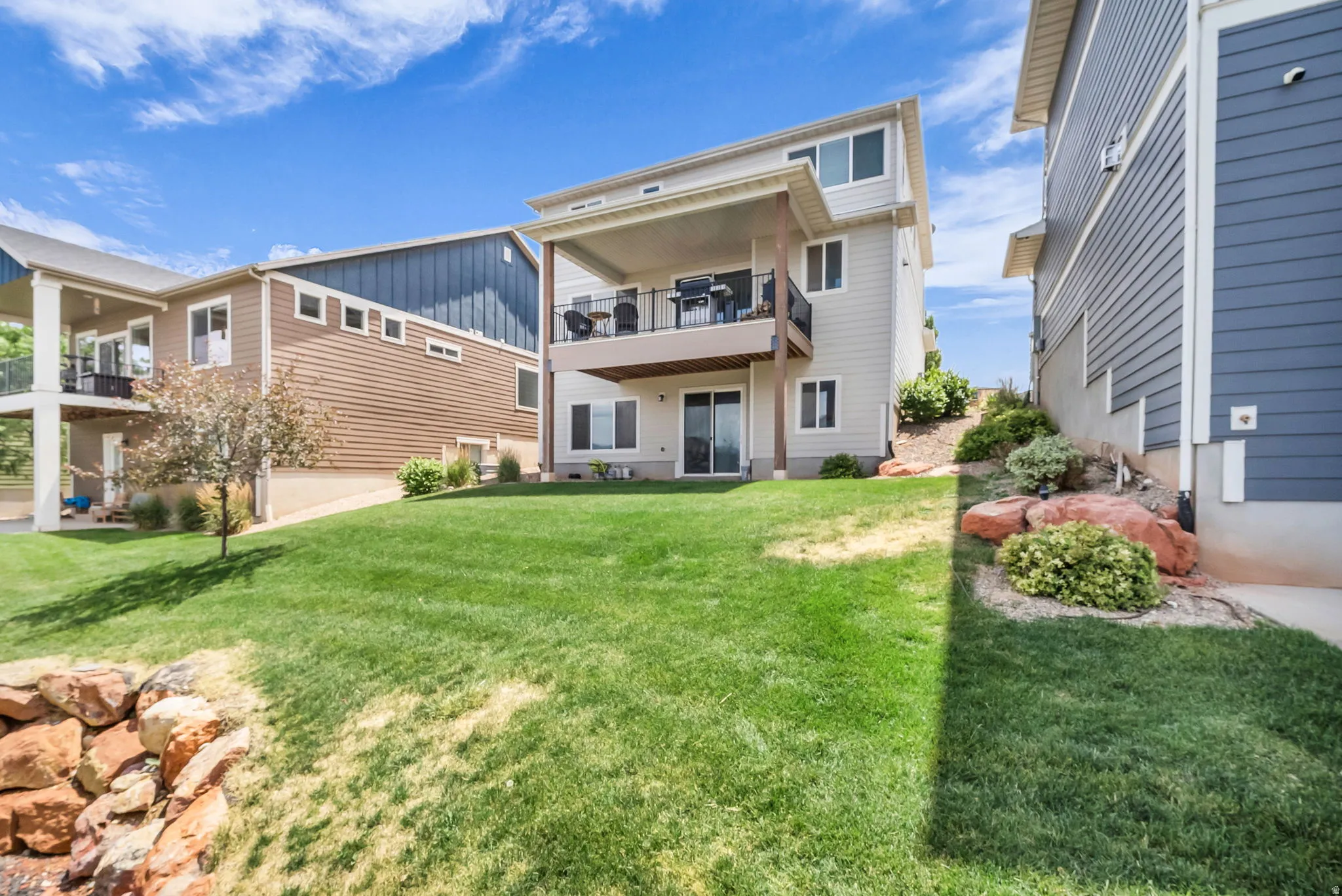 Expansive backyard with a manicured lawn, an upper-level covered balcony, and a lower-level patio with sliding glass door access