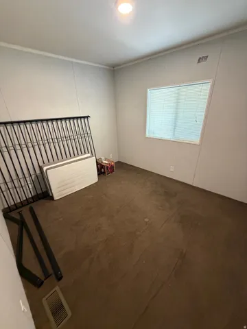 Room featuring neutral wall paneling, crown molding, a window with blinds, brown carpet, and a ceiling-mounted light fixture