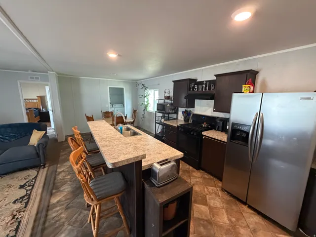Kitchen featuring an island with built-in sink, wood-finish cabinetry, tile-finish flooring, and a stainless steel side-by-side refrigerator
