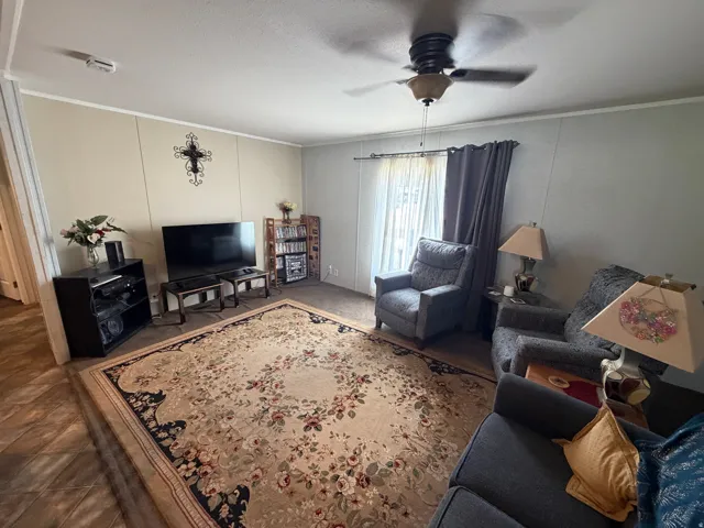 Living area featuring wood-finish flooring, a ceiling fan with integrated lighting, and a large window with privacy coverings