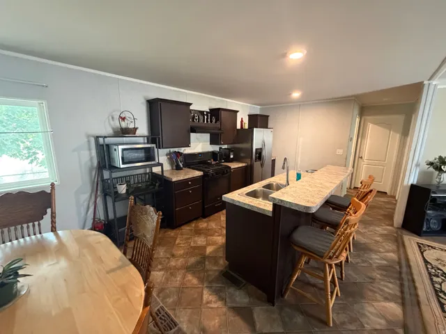 Kitchen featuring dark wood cabinetry, a double basin sink, and a granite-look countertop island with seating