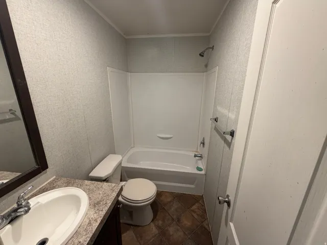 Bathroom featuring a white bathtub with shower, white toilet, and a vanity with a white basin sink