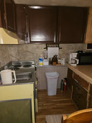Kitchen featuring brown upper cabinetry, a mounted range hood, a stainless steel sink, a four-burner electric range, and wood-finish flooring