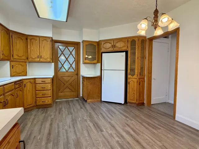 Kitchen featuring wood-finish cabinetry, white countertops, new wood-finish flooring, ceiling light, and chandelier with frosted shades