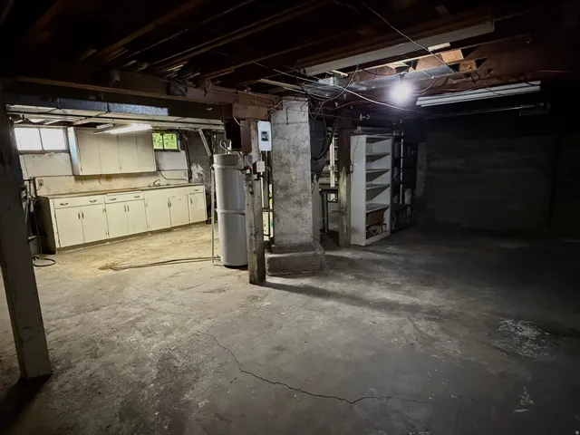 Basement utility space featuring a concrete floor, exposed ceiling joists, and a built-in cabinetry run with a sink
