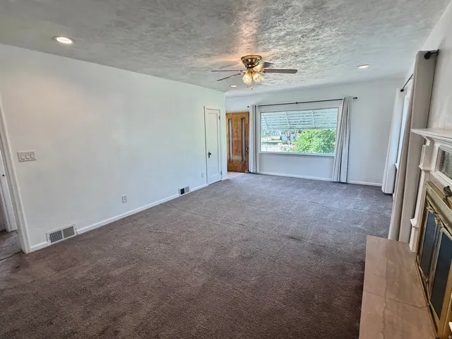 Spacious interior featuring a large window, recessed lighting, a ceiling fan, and a fireplace with a mantel