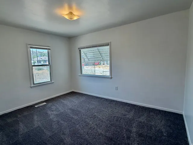 Room featuring two windows with horizontal blinds, neutral wall paint, dark gray carpet flooring, and a flush mount ceiling light fixture
