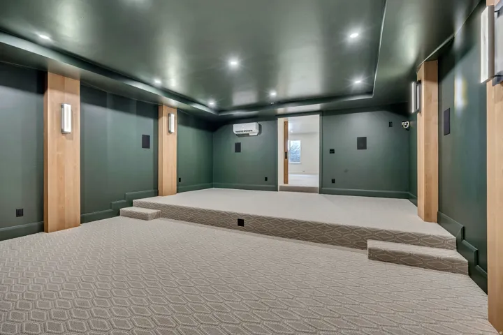 Dedicated entertainment space featuring a raised platform, recessed ceiling lights, and integrated wall speakers