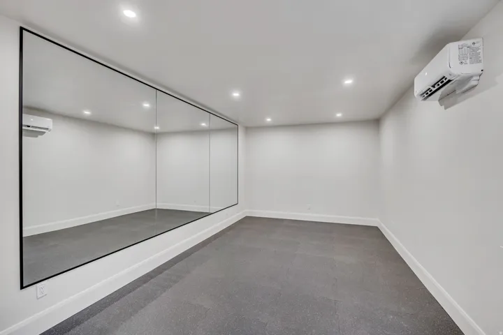 Spacious room featuring a full wall of mirrors, recessed lighting, and wall-mounted climate control unit