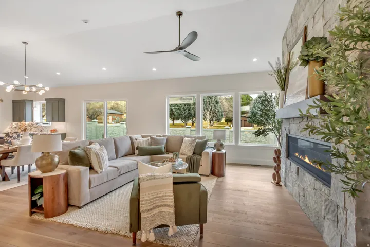 Open-concept living area featuring high quality wood-finish flooring, a contemporary ceiling fan, and a gas fireplace with a stone surround