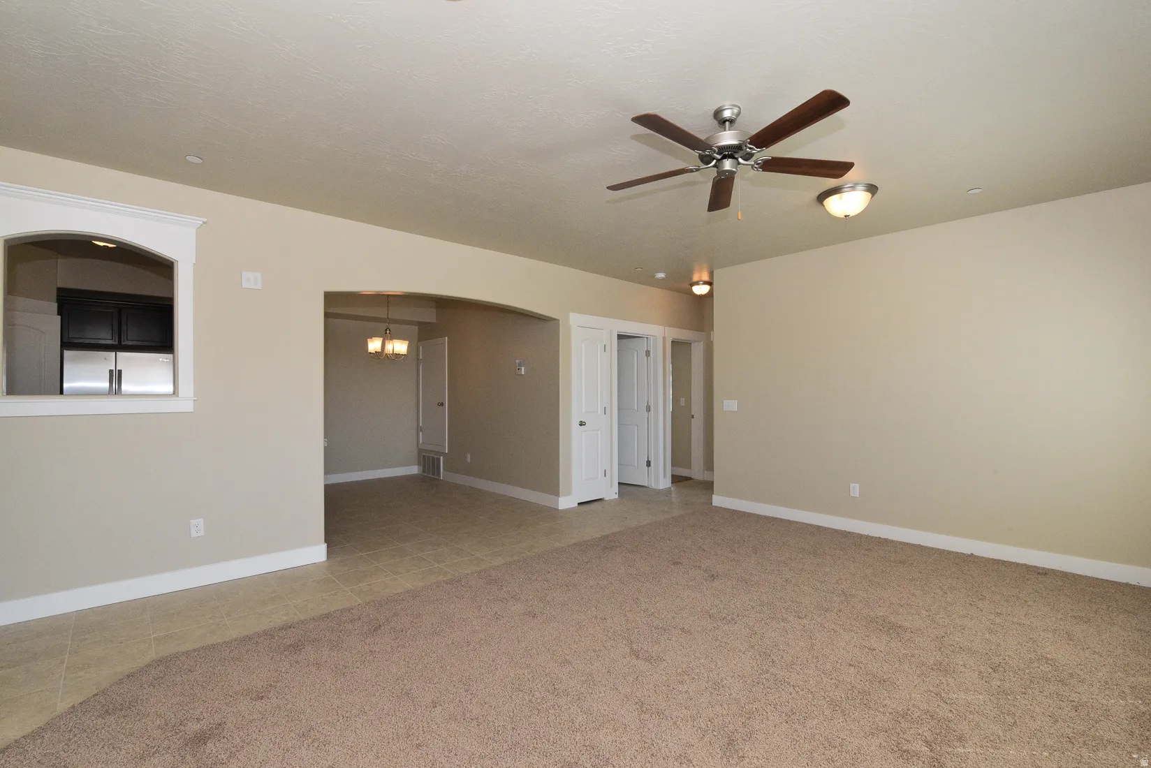 Spacious living area featuring neutral carpeting and a ceiling fan