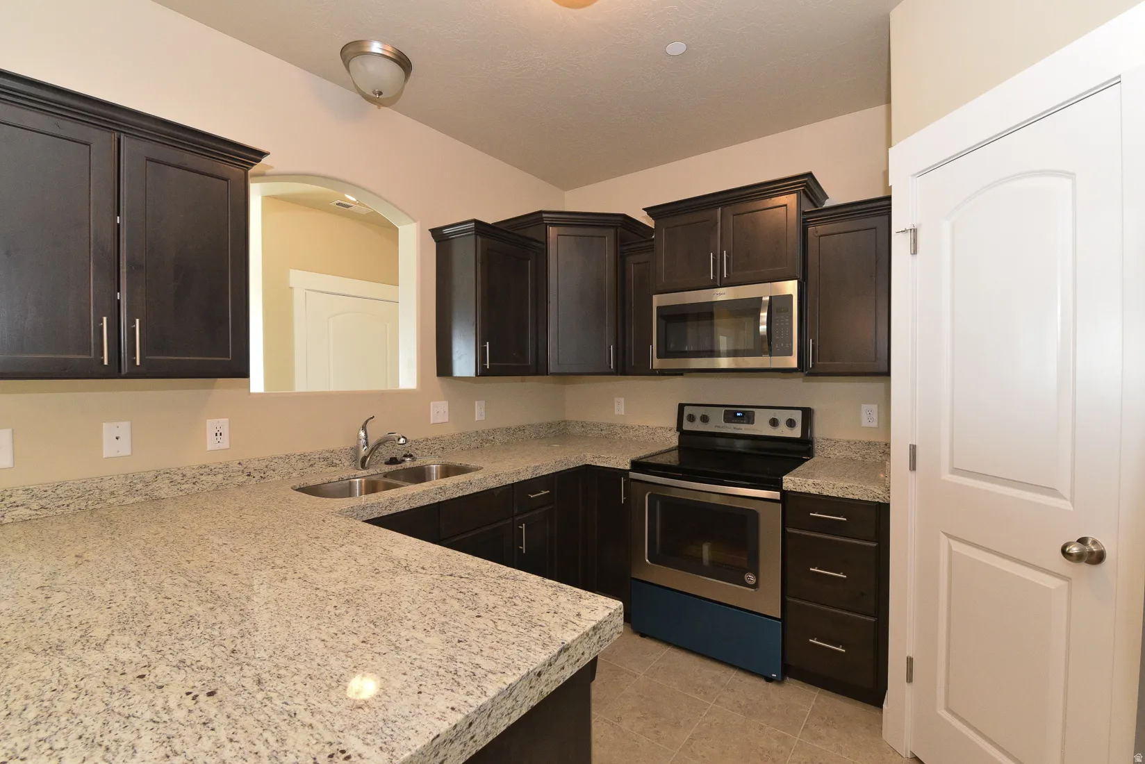 U-shaped kitchen featuring dark wood cabinetry, light speckled countertops, a stainless steel oven with an electric cooktop, and an integrated stainless steel microwave