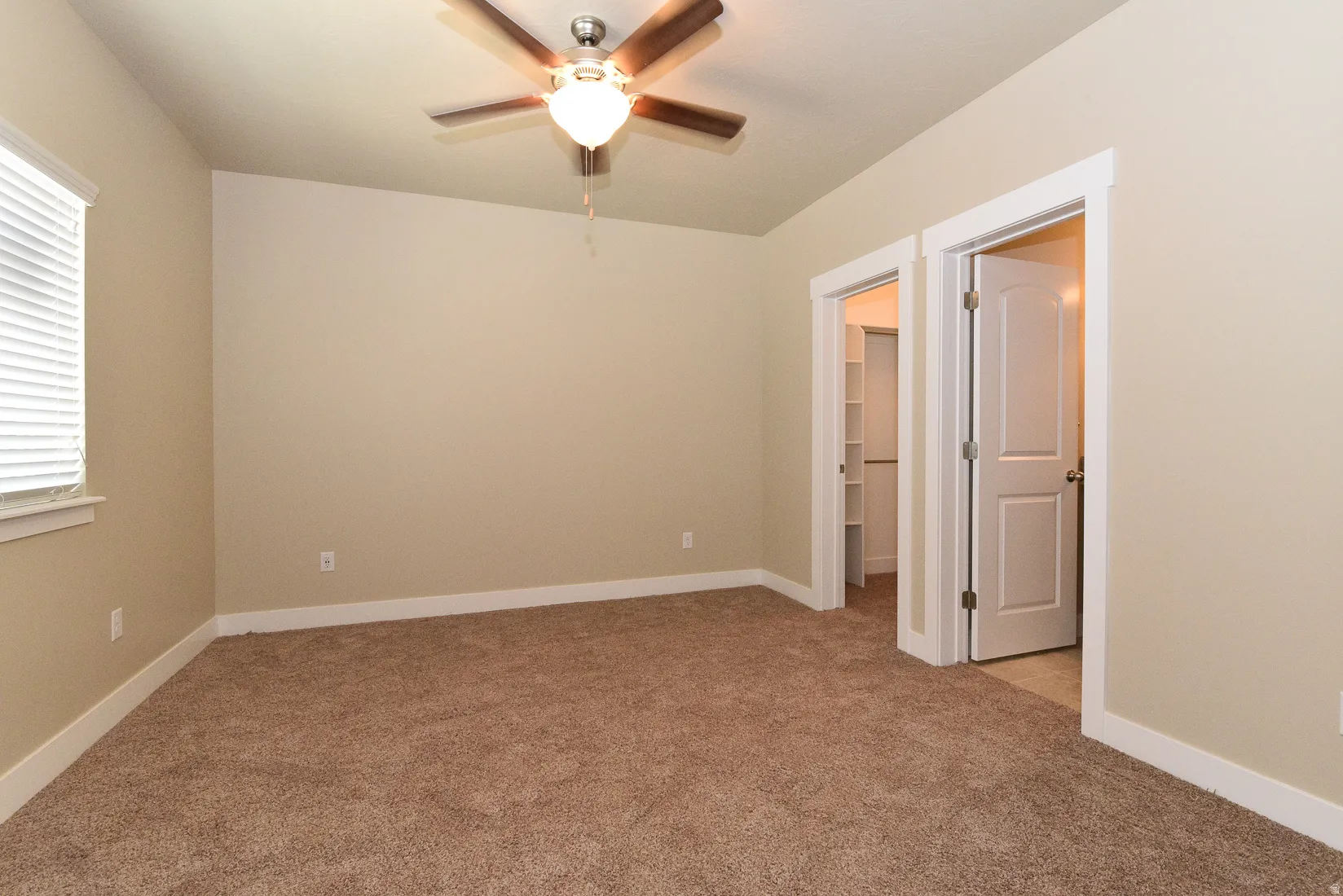 Carpeted room featuring a ceiling fan with integrated lighting, a window with blinds, and two doorways with white trim