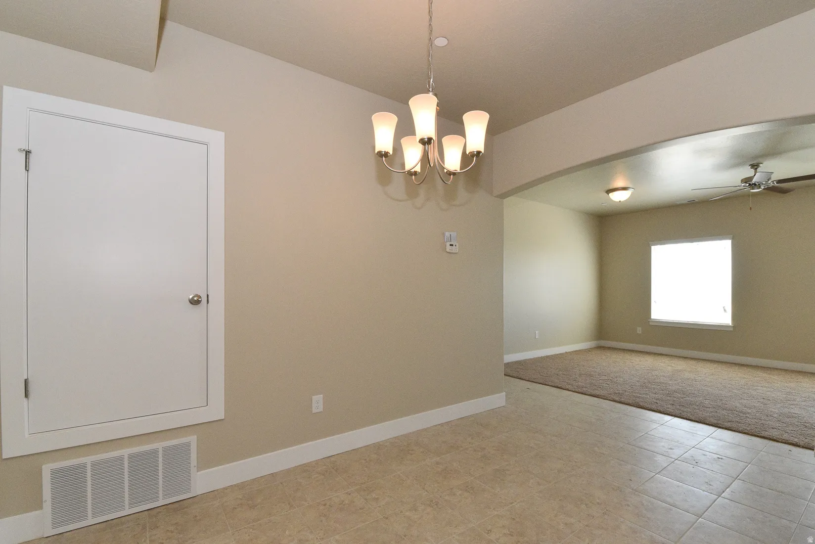 Neutral-toned interior featuring a tile floor, overhead chandelier, and white baseboards