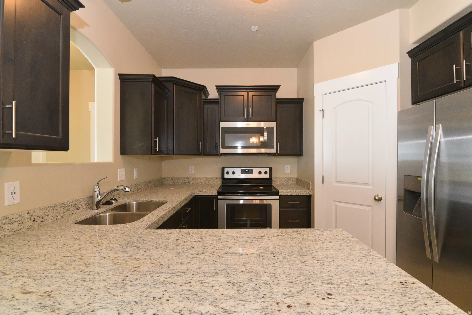 Kitchen featuring dark wood cabinetry, granite countertops, stainless steel appliances, and a double basin sink with a chrome faucet