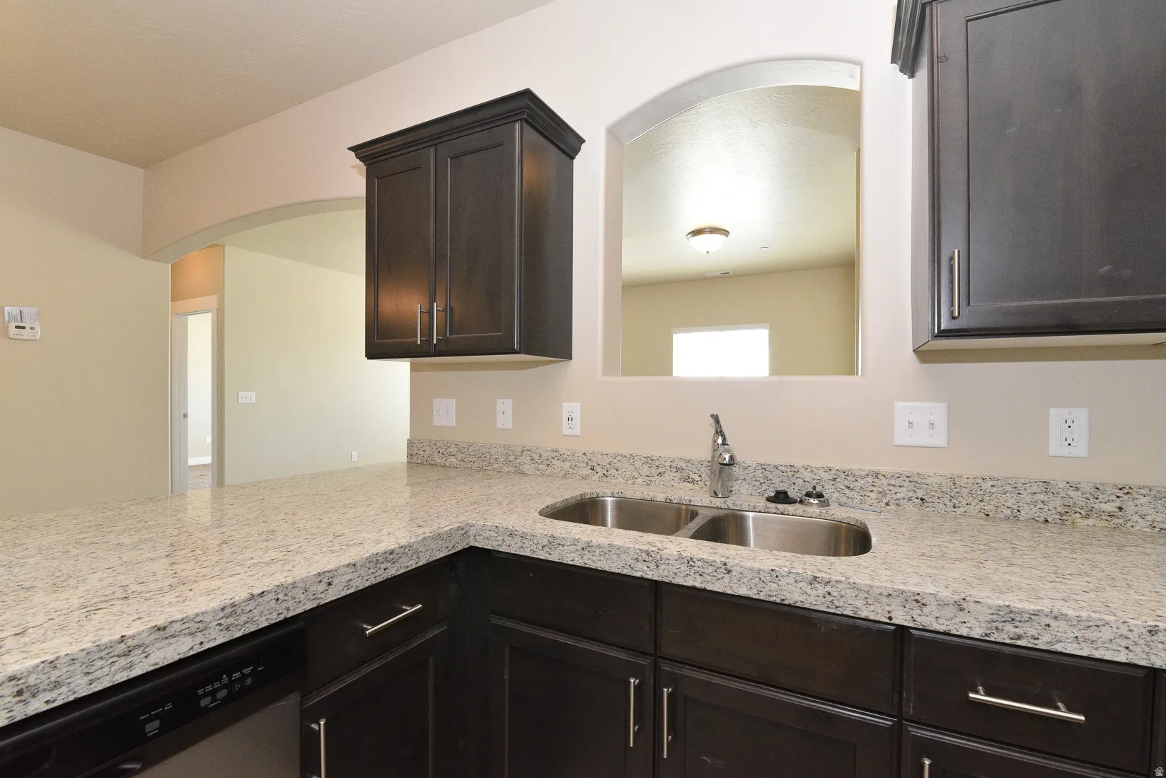Kitchen featuring dark wood cabinetry, light speckled countertops, stainless steel double basin sink, and an arched pass-through window