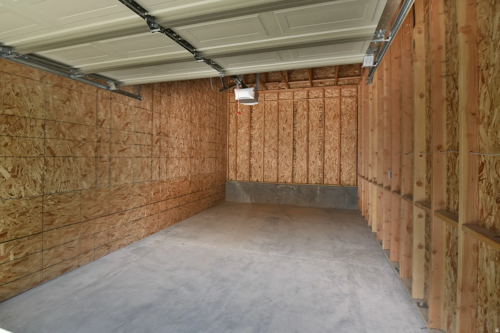 Spacious garage featuring a concrete floor, exposed wood framing, and an overhead garage door mechanism